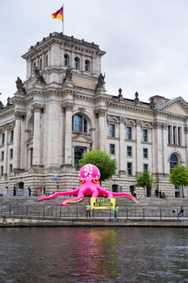 Auf dem Stufen vor dem Reichstag ist ein großer, pinker aufgeblasener Oktopus. Davor stehen Greenpeace-Aktivist:innen und halten ein Banner: "Schützt die Tiefsee".