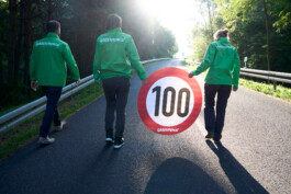 Greenpeace Aktivist:innen tragen eine "100" im Stil eines Verkehrsschildes die Straße hoch.