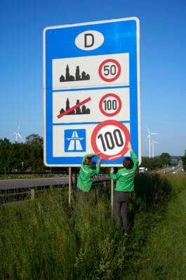 Greenpeace Aktivist:innen kleben eine "100" im Stil eines Verkehrsschildes über das Geschwindigkeitsbegrenzungsschild der Autobahn an der Deutsch-Polnischen Grenze.